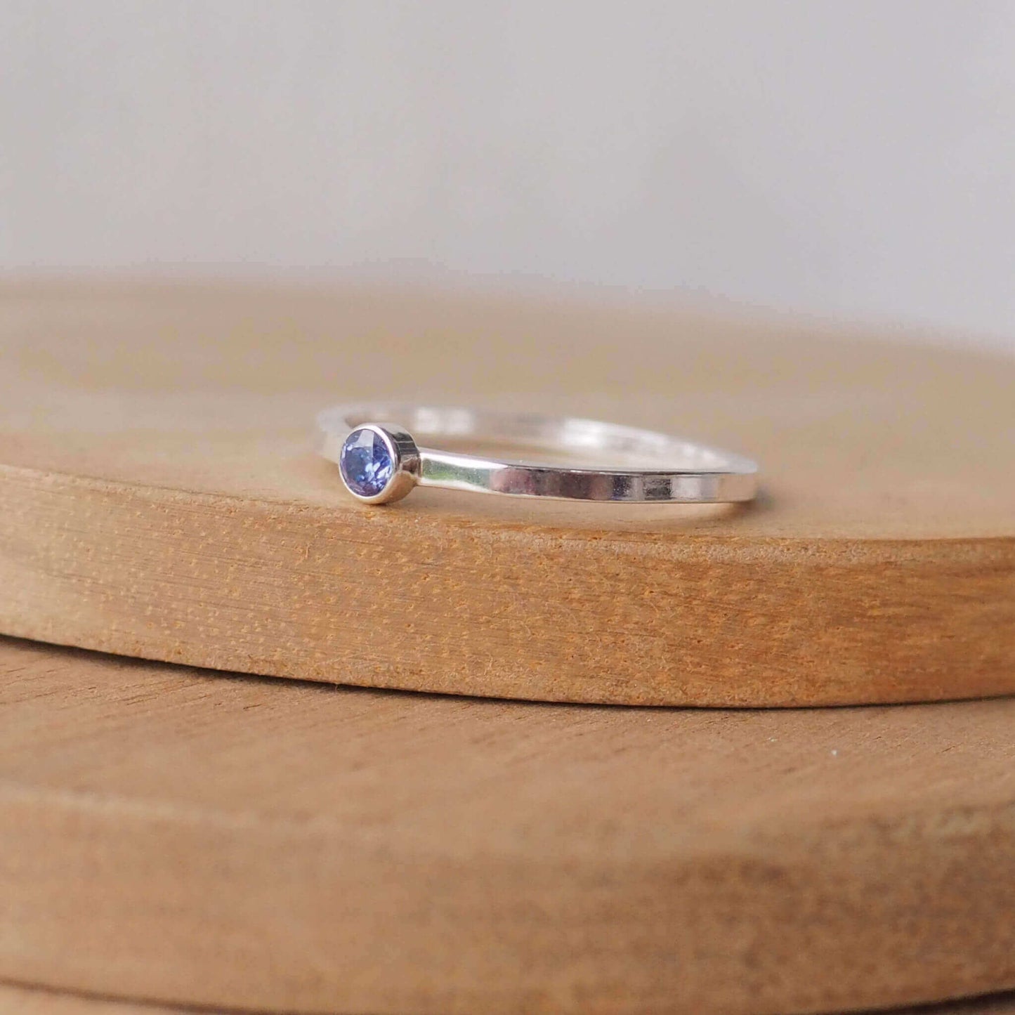 Simple Solitaire ring with a man made tanzanite gemstone. The ring is made from Sterling Silver and a round violet cubic zirconia measuring 3mm in size. It is sent onto a modern ring with a square profile. The ring is handmade by maram jewellery in Scotland