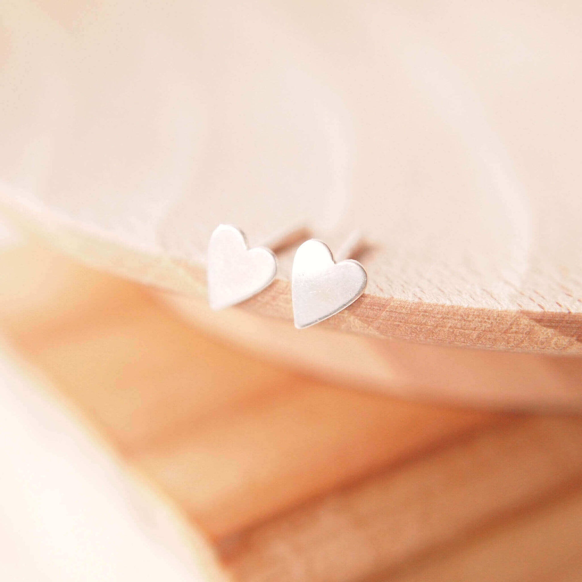 Pair of sterling silver heart earrings handmade by maram jewellery. The earrings are shown on a wooden background