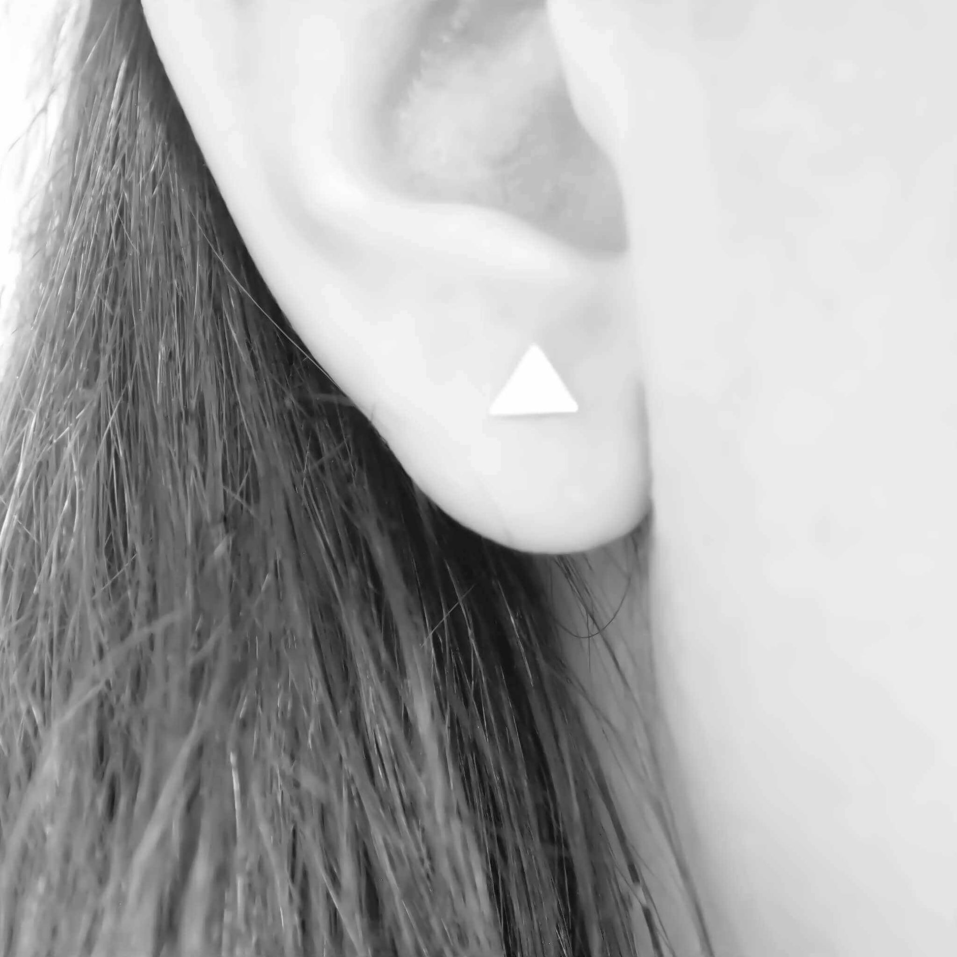 Black and white close up image of an ear with a single piercing showing a small triangle stud. Earrings handmade in Scotland by maram jewellery