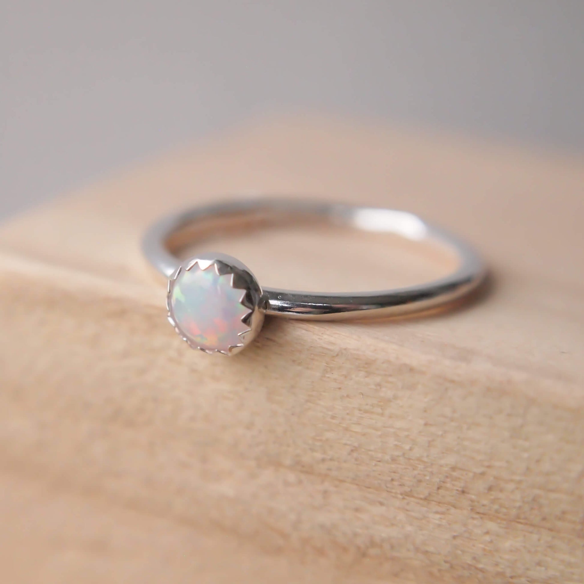 Lab Opal white gemstone and Silver RIng. THe stone is an imitation Opal, round and 5mm in size set onto a simple silver band with a zig zag edge where the silver meets the gem. Handmade by maram jewellery in Edinburgh